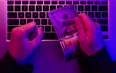 Wall Mural - Money in male hands on the background of a laptop keyboard in neon lighting.