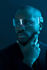 Portrait of a dark-skinned man posing looking to the side with led glasses in a studio with blue lights, smart glasses, display glasses