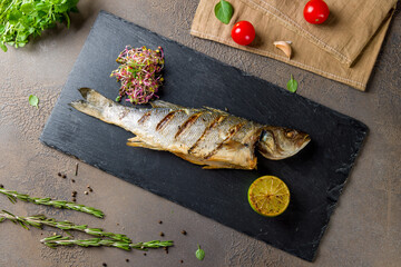 Wall Mural - Fried sea bass on black stone plate with lemon top view