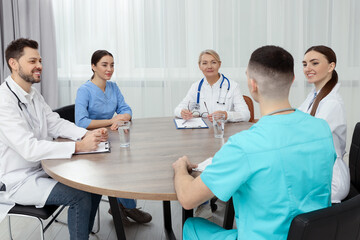 Sticker - Medical conference. Team of doctors having discussion at wooden table in clinic