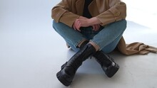 Black Combat Ankle Boots On Tractor Soles With Laces. Close Up. Female Model In Jeans And Coat Demonstrates Warm Footwear.