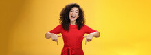 Look What I Got Here. Charismatic Carefree Happy Charming Woman With Curly Hair In Red Dress Laughing With Broad Smile Pointing Down As Showing Awesome Copy Space To Customers Over Yellow Wall