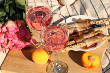 Wall Mural - Glasses of delicious rose wine, flowers and food on white picnic blanket, closeup