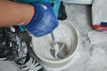 Professional worker mixing plaster in bucket indoors, closeup