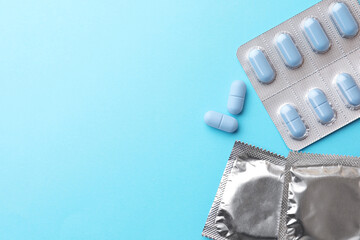 Wall Mural - Pills and condoms on light blue background, flat lay with space for text. Potency problem