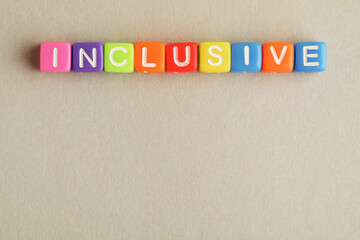 Wall Mural - Colorful cubes with word Inclusive on beige background, flat lay. Space for text