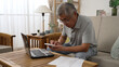 © PRPicturesProduction - Retirement financial planning concept. senior asian man counting on calculator with family budget sitting in living room sofa using laptop computer and paper indoors
