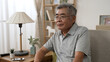 © PRPicturesProduction - Dreamy inspired senior hoary asian man resting on comfortable sofa in morning. serious old male in eyeglasses look front while sitting on couch at home during quarantine.