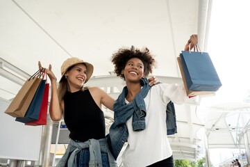 Shopaholic women friends couple lesbian LGBTQ.Beautiful girls in casual  are holding shopping bags, showing paper bag smiling while standing outdoors. Lesbian couple shopping clothes with happiness.