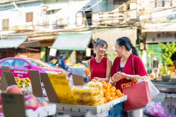 Wall Mural - Happy Asian family mother and daughter choosing and buying fresh fruit orange together at Bangkok Chinatown street market for celebrating Chinese Lunar New Year festive. Chinese culture concept.