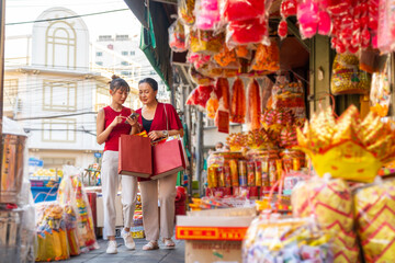 Wall Mural - Asian mother and daughter using navigator on mobile phone while shopping home decorative ornaments and joss paper for celebrating Chinese Lunar New Year festival together at Chinatown street market.