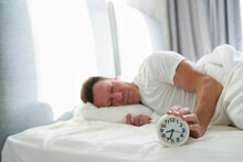 Man Holding Alarm Clock Lying On Bed In Bedroom