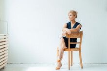 Mature Businesswoman Sitting On Chair In Front Of White Wall