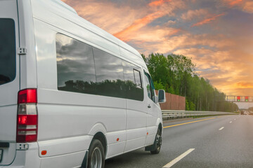 White modern passenger charter van with a small delivery moves fast on the highway to the urban suburbs. Business distribution and logistics express service. Mini bus rides along the highway.