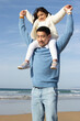 Loving Japanese family walking on beach. Daughter riding on fathers back, looking forward. Leisure, vacation, parenting concept