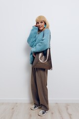 Wall Mural - vertical photo of a beautiful, stylish woman in fashionable earrings and a blue sweater holding a large bag in her hand looking at the camera