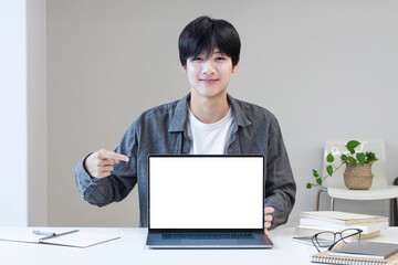 A young college student wears casual clothes and introduces plans and information with a smile, pointing his hand to the laptop screen.