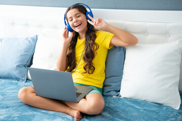 Poster - Happy teen teenage girl in headphones relax on bed at home listen to music using laptop. Child in earphones browse internet on computer, friendship communication. Expressive emotional excited girl.