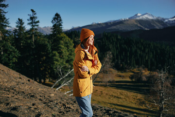 Wall Mural - Woman full-length hiker smiling with teeth standing frozen on the mountain looking at nature happiness mountains and trees in yellow raincoat travel and hiking in the mountains at sunset freedom