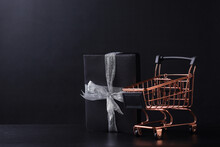 Black Gift Box Using Silver Ribbon With Mini Trolley Isolated On Black Background With Copy Space. 