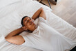 © Drobot Dean - Calm african man lying with his hands under head in bed at home