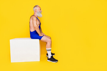 Sticker - Side profile photo of bodybuilder grandfather wear blue costume sportive sitting white box rest look ad isolated on yellow color background