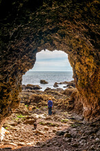 Looking Through Archway Of A Limestone Cave On Marsden Beach To A View Of A Woman Going For A Walk With Her Dogs Along The Shore Of The North Sea; South Shields, Tyne And Wear, England, United Kingdom