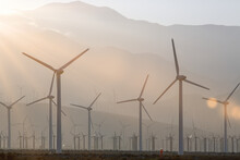 Wind Farm With Wind Turbines At Sunset, And An Engineer In Red Coveralls Stands Doing An Inspection; Palm Springs, California, United States Of America