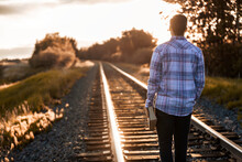 A Young Man Stands On Train Tracks Holding His Bible And Looking Up The Tracks; Alberta, Canada