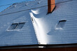 Closeup of house roof top with attic windows covered with snow in cold winter. Tiled covering of building in wintertime weather
