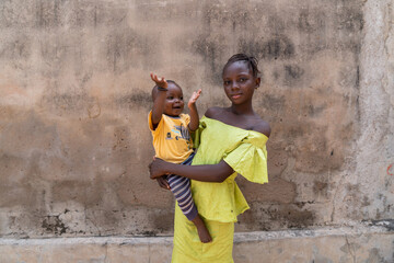 Beautiful young African girl holding her laughing little brother in her arms, symbolizing traditional family ties