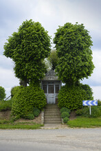 Steps Leading To Small Chapel Surrounded By Chestnut Trees With A Blue And White Chevron Sign On A Road Near Arras; Northern France, France