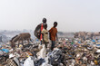 Three African street kids standing in a steaming dump looking for recyclable items to sell