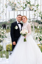Happy Couple On Wedding Day Posing On Flowering Altar Outdoors