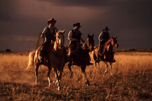 Three Cowboys Roping On Horseback With Ominous Storm Clouds Overhead; Seneca, Oregon, United States Of America