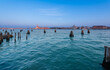 View of pilings in the lagoon and buildings along the shoreline; Venice, Veneto, Italy