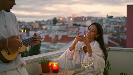 Wall Mural - Brunette lady photographing smartphone terrace. Handsome man playing ukulele