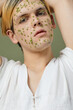 © Clique Images - Low angle view portrait of feminine guy posing with beauty mask and tiny green flowers on his face