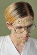 © TrueFrame Collective - High angle view close-up portrait of queer model with green flowers on face wearing glasses