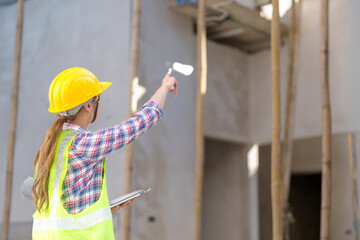 Asia Female civil engineer with inspecting construction plans at building site of high-riser building site survey in civil engineering project.