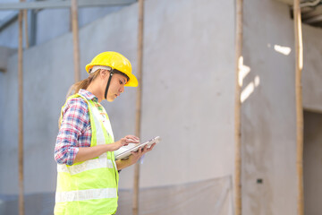 Asia Female civil engineer with inspecting construction plans at building site of high-riser building site survey in civil engineering project.