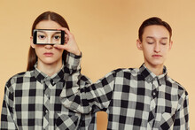Pretty Androgynous Female In Checkered Shirt Holding Smartphone With Eyes Photo Near Face Of Handsome Man While Standing Against Brown Background Together
