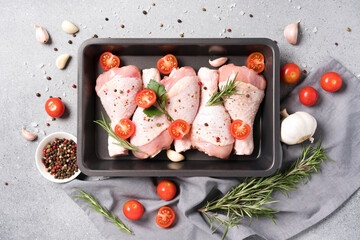 Wall Mural - Cooking chicken legs in black baking form with seasonings and tomatoes over gray concrete background. Raw chicken drumsticks ready to cook. Organic meat, healthy eating concept