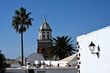 Der Kirchturm von Teguise auf Lanzarote, ragt zwischen Palmen in den blauen Himmel.