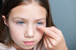 Little child girl putting contact lens into her eye, closeup
