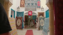 Man Entering A Carpet Market With Colourful Handicraft Carpets. Carpet Trade In Tunisia In Different Colours And Shapes. Traditional African Rugs.