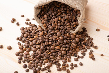 Canvas Print - Roasted coffee beans falling from linen bag on wooden table. Beautiful composition of coffee grain