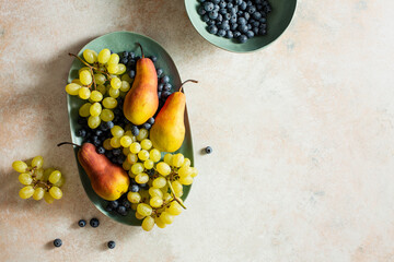 Wall Mural - Ripe pears, green grapes and blueberries in a blue flat plate.