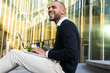 © ADDICTIVE STOCK - Concentrated happy businessman using laptop outside building