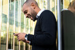 © ADDICTIVE STOCK - Black businessman messaging on cellphone standing against modern office building